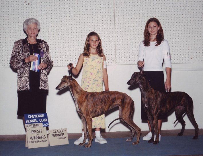 Three women and two dogs are standing in front of a sign.